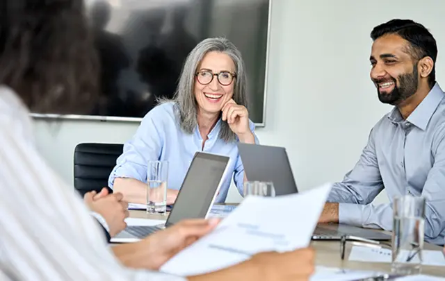 A group meeting with four people at a table. Two are smiling, discussing documents.