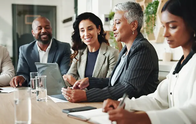 Five professionals seated around a table in a modern office, engaged in a collaborative discussion. 
