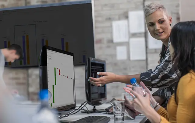 Two professionals in an office setting collaborate in front of desktop monitors