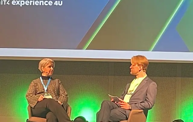 Two speakers seated on stage at a professional event, engaged in a discussion. 
