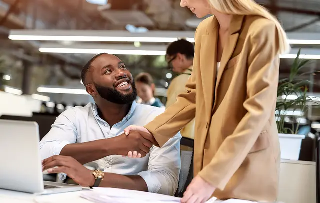 Two professionals in a modern office setting engage in a handshake, symbolizing collaboration or agreement. 