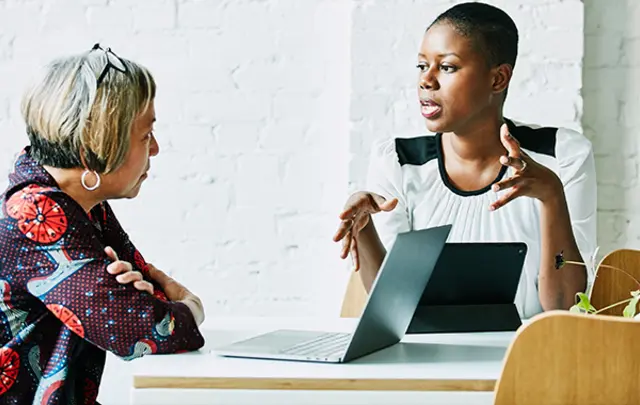 Two women seated at a modern table in a professional setting. 