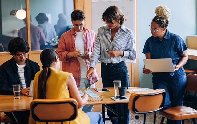 Five individuals gathered around a wooden table in a modern office setting.