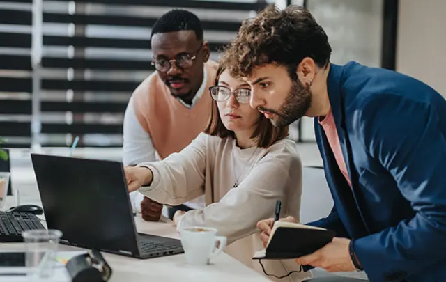 Three colleagues collaborating around a laptop in a bright, modern office setting.