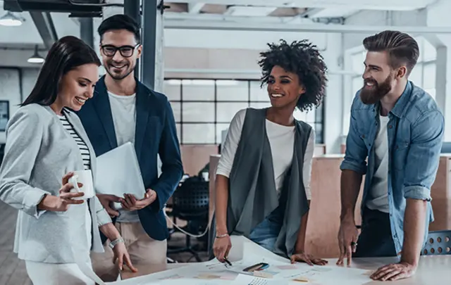 Four colleagues gathered around a table in a modern office, engaged in a collaborative discussion. 