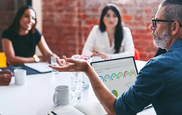 A modern office setting with four individuals seated around a round white table, engaged in a collaborative discussion.