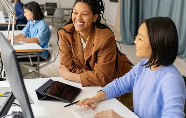 Two women collaborate at a desk in a bright, modern office.