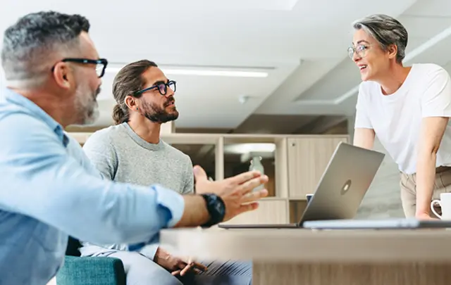 Three colleagues collaborate around a light-colored table in a modern office.