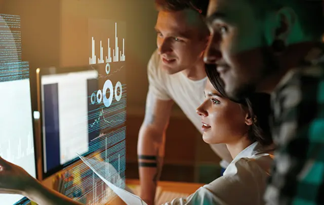 Three professionals collaborate in a dimly lit, high-tech workspace.