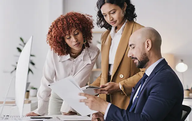 Three professionals collaborate around a light-colored desk in a modern office.