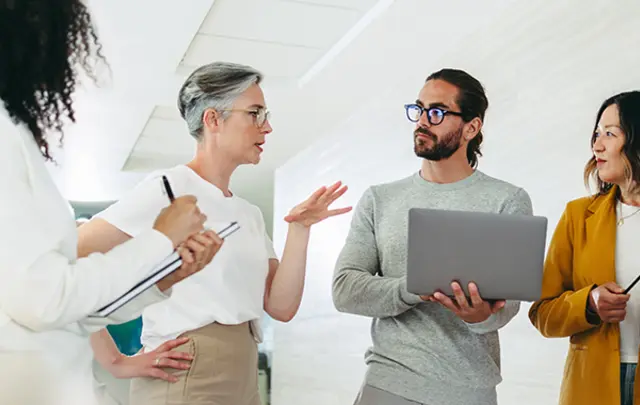 Four colleagues engage in a collaborative discussion in a modern office setting.