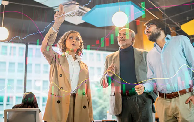 Three professionals in a meeting discussing graphs and data on a screen.