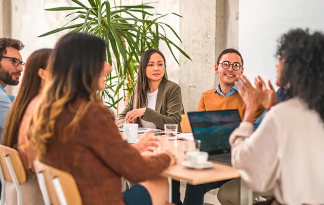 Six professionals collaborate around a light-colored table in a modern office. 