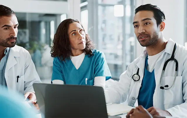 A group of medical professionals discussing in front of a laptop in a bright room
