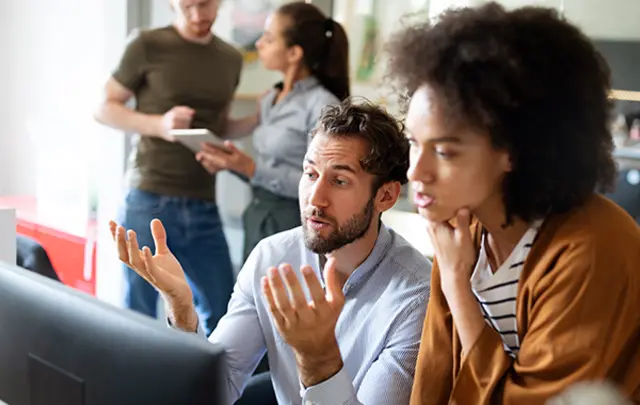 A man and a woman collaborate in a modern office, focused on a computer monitor. 