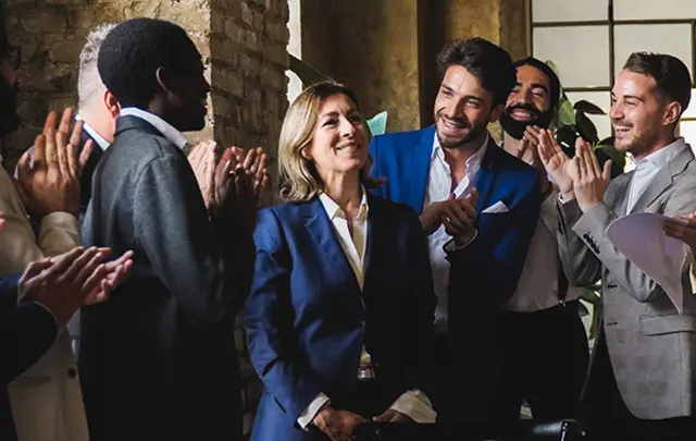 A group of people applauding a woman in a suit, celebrating a success in a bright room. 
