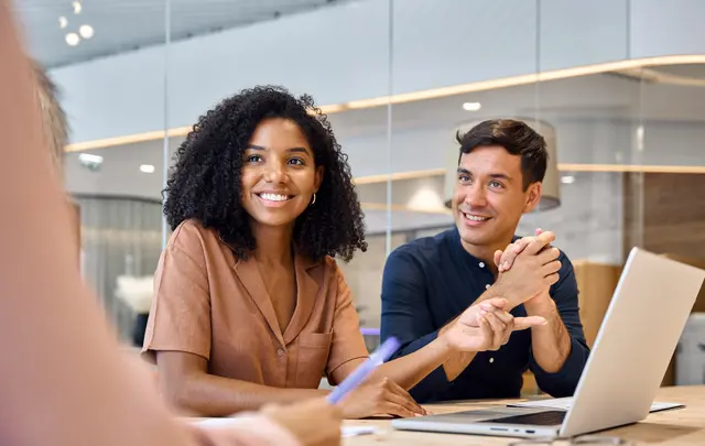 Two people in a meeting, smiling and discussing with a laptop on the table. 