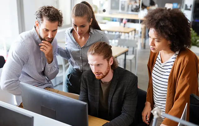 Four people gathered around a computer, looking intently at the screen in an office setting