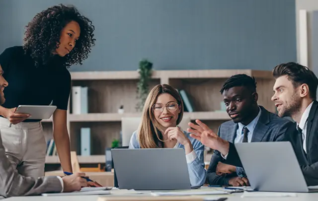A diverse group of professionals discussing ideas around a laptop in a modern office. 