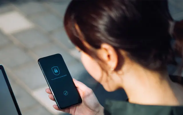 A person is holding a smartphone displaying a lock icon and a security-related interface, suggesting device protection or authentication.