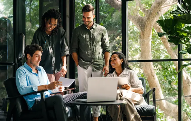 A group of four people are gathered in a modern office space with large windows and abundant natural light. 