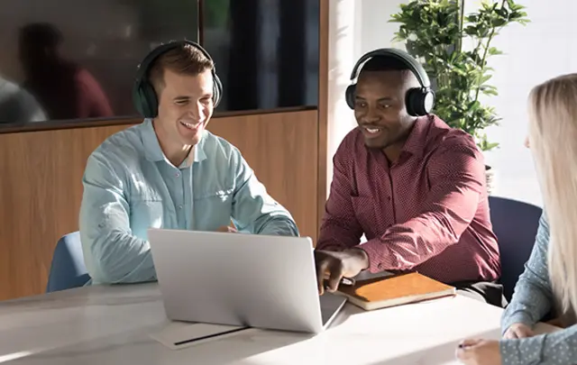 Three colleagues sit around a table in a modern office, collaborating during a video or online meeting. 