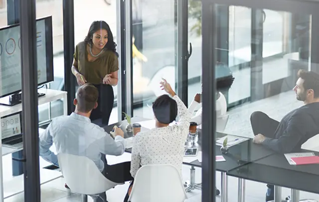 Eine Gruppe von Fachleuten diskutiert in einem modernen Besprechungsraum über Daten, die auf einem Präsentationsbildschirm angezeigt werden.