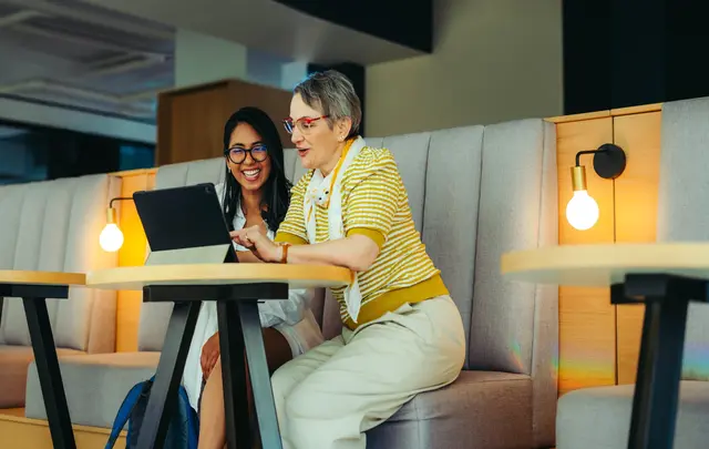 Two professionals collaborate at a tablet while seated in a modern office lounge area. 