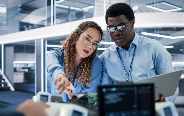 Two professionals reviewing data and technology equipment in a modern office environment
