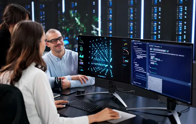 Team members reviewing AI analytics and data visualizations on multiple computer screens in a modern office.