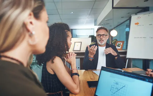 Business professionals collaborating in a modern meeting room, with one participant presenting ideas during a strategic sourcing or procurement discussion while colleagues listen around a conference table.
