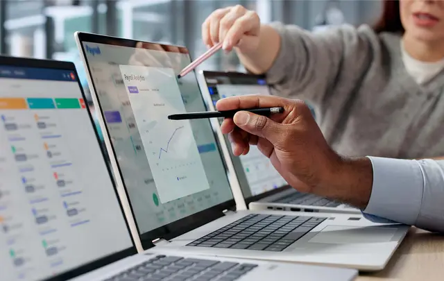 Close-up of business professionals reviewing payroll analytics on multiple laptop screens, pointing to charts and data visualizations during a collaborative discussion about workforce planning, reporting, and operational efficiency.