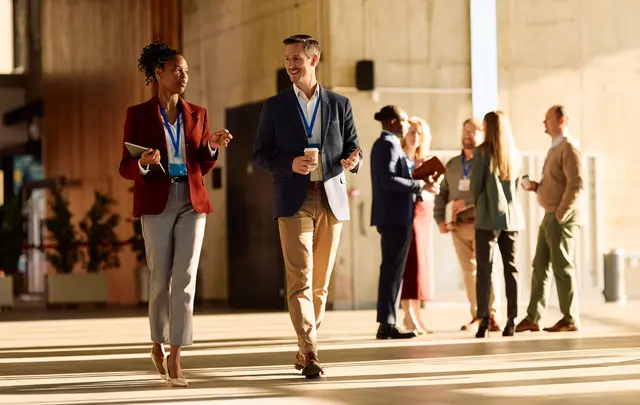 Business professionals wearing conference badges walk and network in a modern event venue.