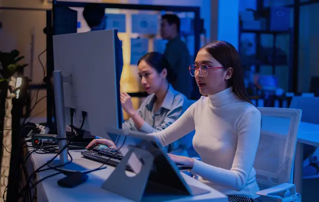 Person working at a computer workstation in a modern office environment, with multiple monitors and a tablet on the desk.