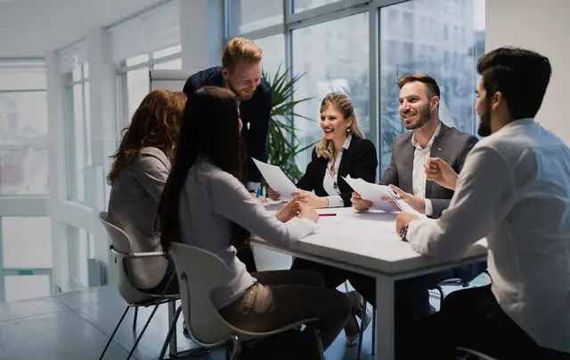 Team members gathered around a conference table reviewing documents during a collaborative finance and planning meeting in a modern office with large windows and natural light.