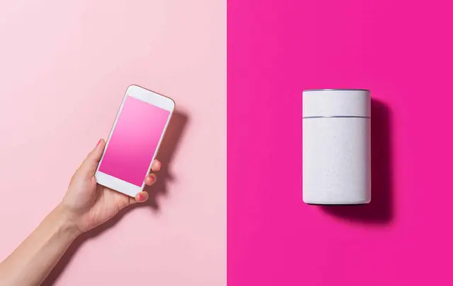 a hand holding a mobile phone close to a home speaker