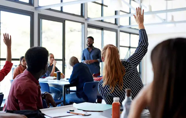 a university classroom with several students with their hands up