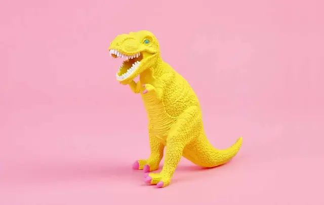 a yellow dinosaur toy on a pink background