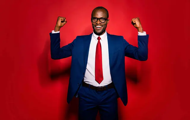 a young smartly dressed man in a red tie celebrating in front of a red background