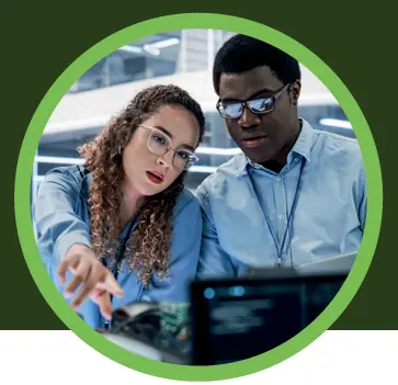 Two colleagues collaborating in a modern office, reviewing data on a laptop and pointing at a screen, highlighting analysis and data-driven decision-making.