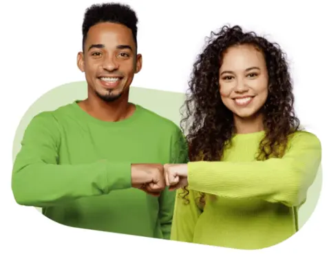 Two smiling people wearing green sweaters, fist-bumping each other. 