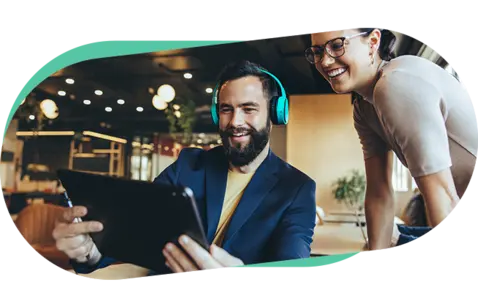 A man in a blue jacket and turquoise headphones smiles while using a tablet, with a woman beside him