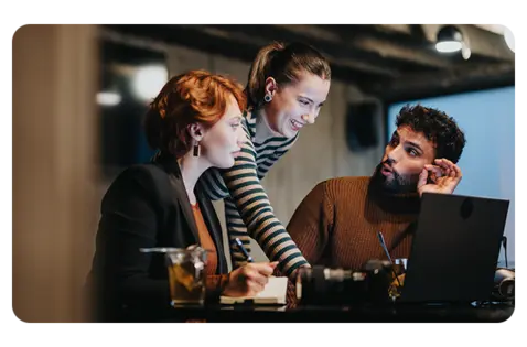 Copilot said:  Alt text:  Three colleagues collaborating at a desk in a modern office, reviewing information on a laptop during a team discussion.