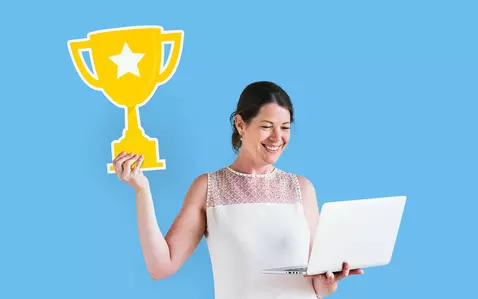 Picture of smiling woman holding a cartoon trophy in one hand and a laptop in the other