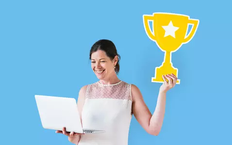Smiling woman holding laptop in one hand and trophy in her other hand