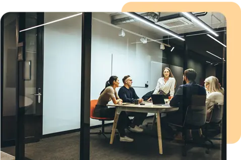A modern office meeting room with five people gathered around a rectangular table. 