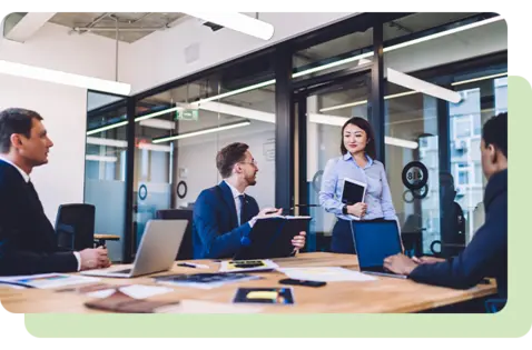 Team of professionals collaborating around a meeting table in a modern office, with laptops and notebooks as one person presents ideas while others listen and discuss.