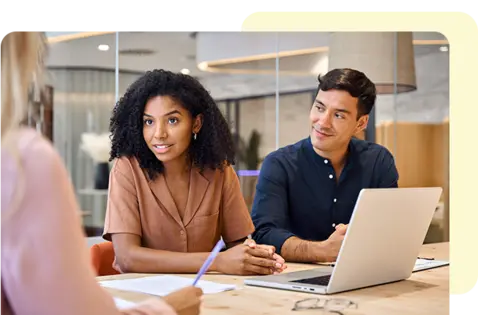 Drei Kollegen sitzen an einem Tisch in einem modernen Büro und besprechen Dokumente und Informationen an einem Laptop während eines Meetings.