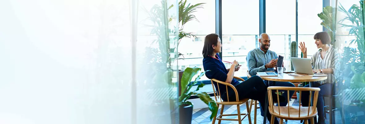 three people talking around a circular table which has their laptops resting on it