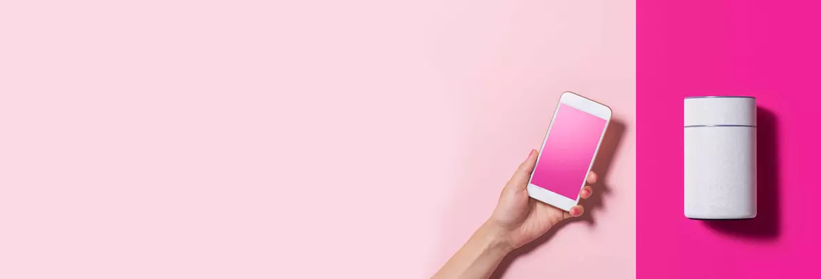 a hand holding a mobile phone close to a home speaker